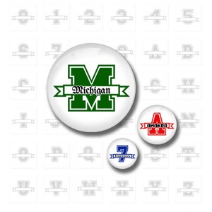 May include: A set of 26 round, white buttons with a gray outline. Each button features a large, bold letter or number with a banner underneath. Some buttons have text on the banner, such as "Michigan" and "Amanda".