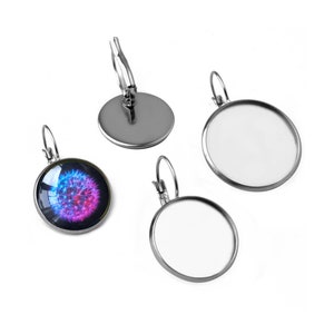 May include: A set of four silver-toned earring blanks. Two blanks are empty and two blanks have a round glass cabochon. One cabochon has a colorful dandelion design.