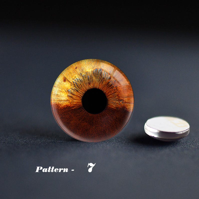 May include: A round, glass eye with a detailed iris pattern in shades of brown and gold, with a black pupil. A small, white and silver object is next to the eye. The text "Pattern - 7" is at the bottom.