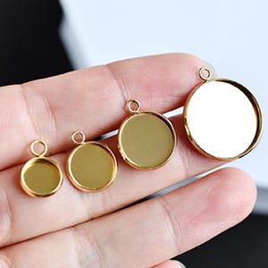 Puede incluir: Cuatro colgantes redondos dorados de diferentes tamaños, cada uno con un pequeño lazo en la parte superior para sujetarlo a una cadena o cordón. Los colgantes tienen una superficie brillante y reflectante.