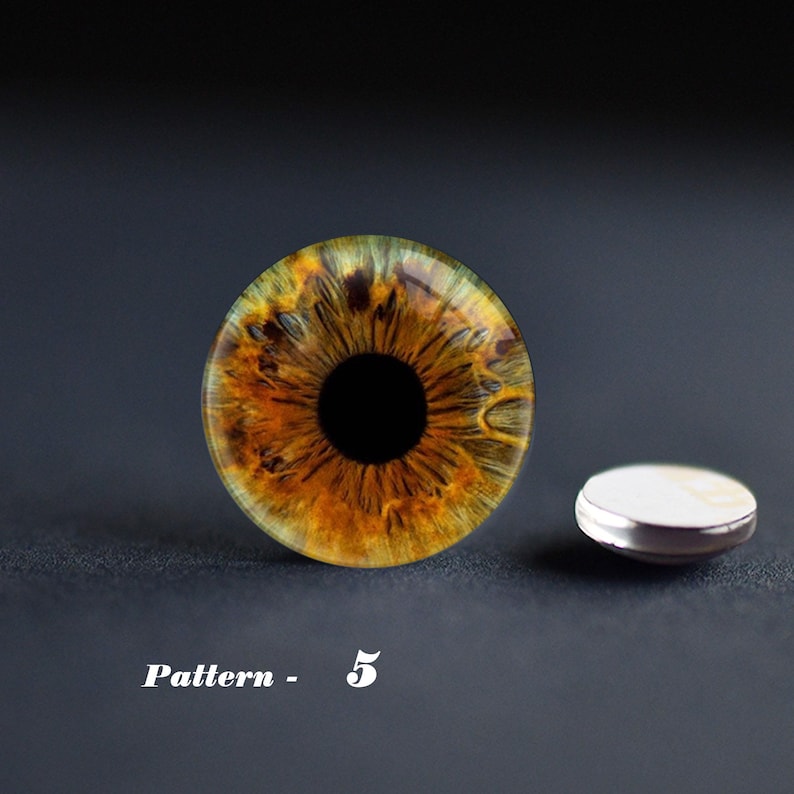 May include: A detailed close-up of an eye with a brown and yellow iris and a black pupil. The eye is next to a small, round, silver-rimmed object. The text "Pattern - 5" is below the eye.