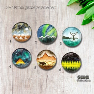 May include: Six round glass cabochons with different nature-themed designs. The designs include a snowy mountain range, a green aurora borealis, a whale tail in the ocean, a teepee under a starry sky, a buffalo in a field, and a forest with yellow and black stripes.