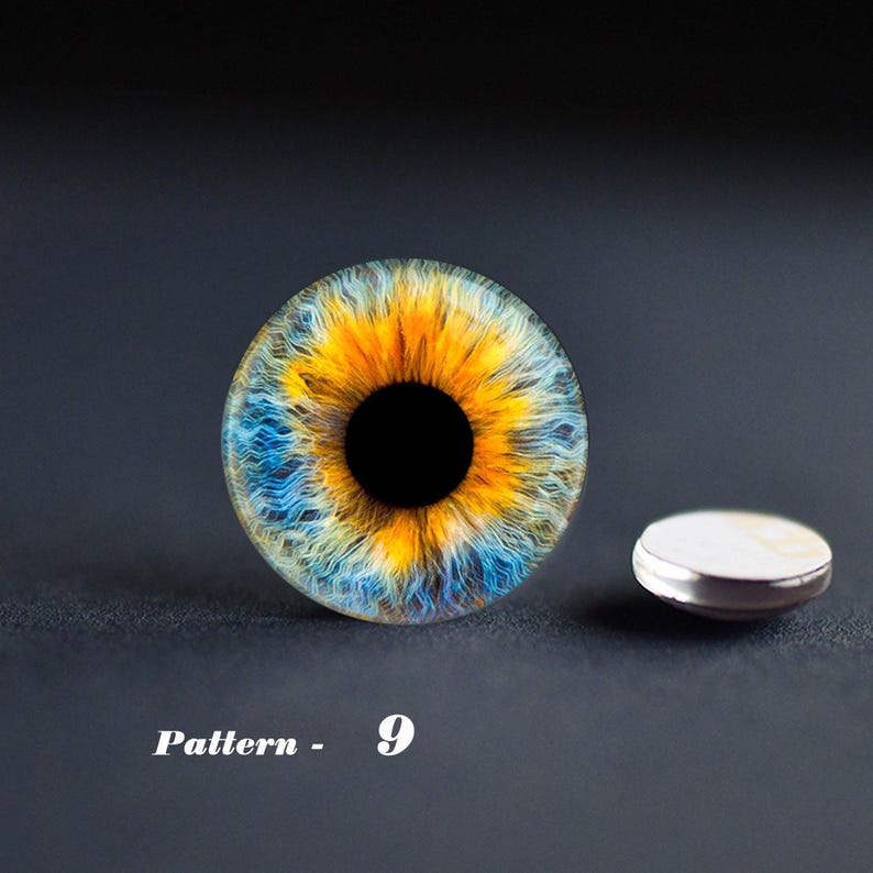 May include: A detailed, close-up of an eye design with a vibrant mix of colors. The iris features a striking pattern of yellow, blue, and orange hues, with a black pupil. A small, silver-rimmed object is next to the eye. The text "Pattern - 9" is below the eye.