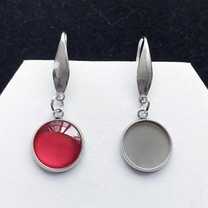 Könnte beinhalten: Ein Paar silberne Ohrhänger mit runden Glascabochons. Ein Ohrring hat einen roten Cabochon und der andere einen grauen Cabochon.