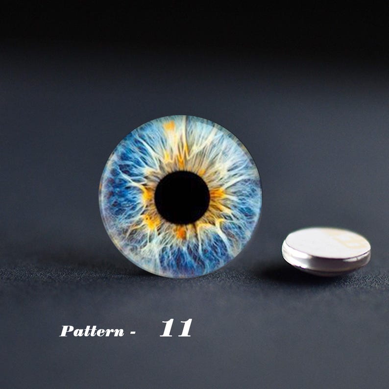 May include: A detailed close-up of a blue and yellow eye pattern, with a black pupil. A small, round, silver-rimmed object is next to the eye design. The text "Pattern - 11" is below the eye design.