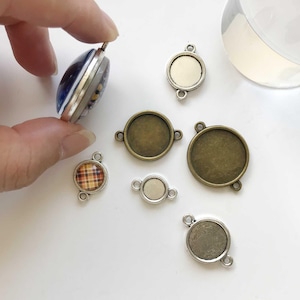 Op de afbeelding: Assortiment ronde metalen bezel settings voor het maken van sieraden. De bezels zijn in zilver en brons tinten, sommige met een geruit patroon.