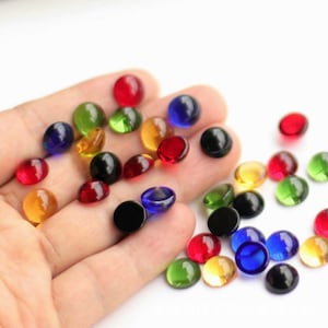 May include: Assortment of colourful glass cabochons in various colours, including red, green, blue, yellow, and black. The cabochons are round and have a smooth, polished surface.