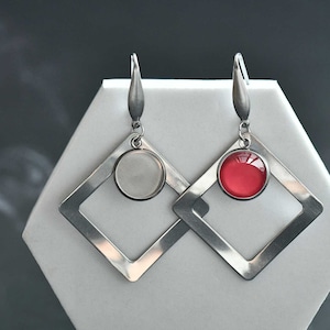 May include: A pair of silver earrings with a square frame and a round, coloured glass insert. One earring has a white insert, and the other has a red insert.