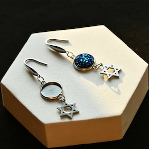 May include: A pair of silver earrings with a blue glitter charm and a silver star of David charm.