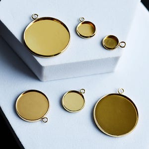 Puede incluir: Una colecci&oacute;n de bandejas colgantes doradas de varios tama&ntilde;os. Las bandejas son redondas con un peque&ntilde;o lazo en la parte superior para sujetar una cadena. Las bandejas est&aacute;n vac&iacute;as y listas para personalizar. El fondo es blanco y negro.