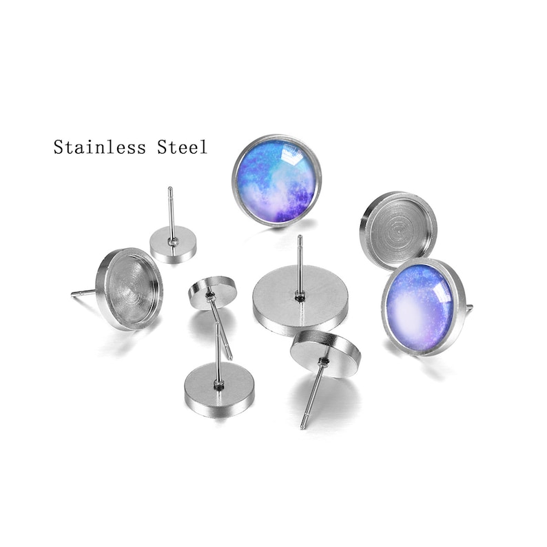 May include: A set of six stainless steel earring posts with round, silver-colored bases and a single post. Three of the posts have a clear glass cabochon, and three have a blue and purple galaxy-themed cabochon.