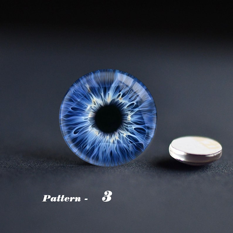 May include: A blue eye-shaped glass cabochon with intricate white and blue patterns, next to a small, round, silver-rimmed object. The text "Pattern - 3" is visible below the cabochon.