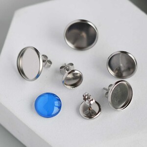 Può includere: Un set di sei montature per orecchini in argento con bezel rotondi. I bezel sono vuoti, ma uno di essi contiene un cabochon di vetro blu.
