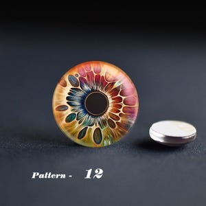 May include: A colorful, eye-shaped design with a black center and intricate patterns in shades of orange, pink, blue, and green. A small, silver-rimmed, white-topped object sits beside it. The text "Pattern - 12" is at the bottom.