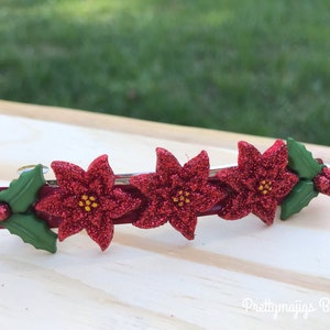 May include: Red glitter poinsettia hair clip with green holly leaves. The clip is made of plastic and has a metal bar.