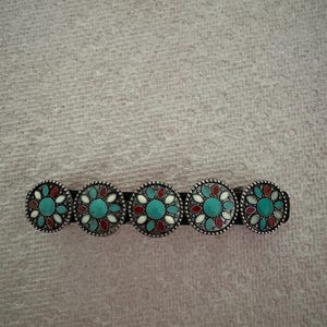 May include: A silver belt buckle with five round turquoise, red, and white stones.