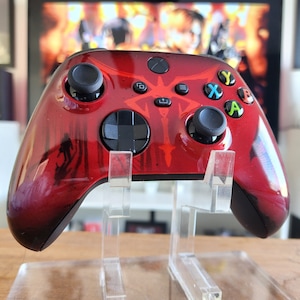 May include: A red Xbox controller with a black and white design. The controller is on a clear stand.