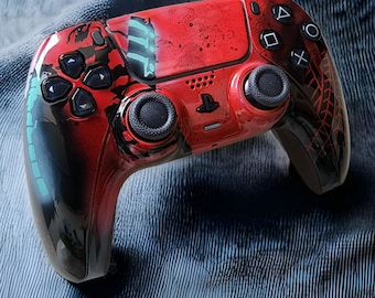 Puede incluir: Un mando de PlayStation 5 DualSense personalizado en rojo y negro con un diseño abstracto azul y verde. El mando tiene una superficie texturizada y un patrón de telaraña negra en la parte posterior.