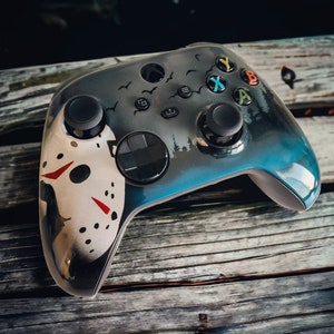 Op de afbeelding: Een zwarte en blauwe Xbox-controller met een wit en rood Jason Voorhees-maskerontwerp. De controller heeft een blauw en zwart kleurenschema met een wit en rood Jason Voorhees-maskerontwerp.