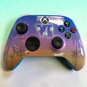 May include: A wireless video game controller featuring a gradient color scheme transitioning from blue at the top to purple and orange at the bottom. The surface displays a silhouette of palm trees and the Roman numeral VI in the center.