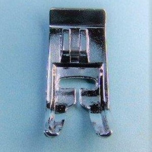 Könnte beinhalten: Nahaufnahme eines silbernen Nähmaschinen-Nähfußes. Der Fuß hat eine rechteckige Oberseite mit drei vertikalen Stäben und zwei gebogenen Füßen. Das Metall reflektiert das Licht. Für Nähen und Basteln.