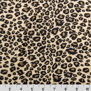 May include: Close-up of a fabric with a leopard print pattern. The fabric has a beige background with dark brown and black spots. The pattern is evenly distributed across the surface, creating a textured appearance. The fabric is measured in inches.