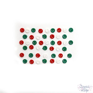 May include: Assortment of small, round buttons in red, white, and green colors. The buttons are scattered on a white surface.