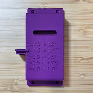 May include: A vibrant purple tool with a rectangular body and a horizontal slot. The tool has a small, protruding handle on the side. Text on the tool indicates measurements: 2.0 -> 1.0", 2.5 -> 1.25", 3.0 -> 1.5", 3.5 -> 1.75", and 4.0 -> 2.0".
