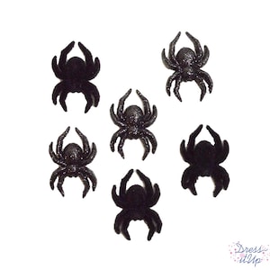 May include: Six black glittery spider embellishments arranged on a white background. The spiders have eight legs and are in various poses. The image is suitable for Halloween or craft projects.