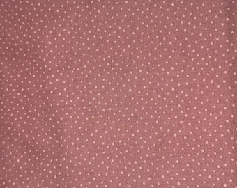May include: Close-up of a dusty rose fabric with a repeating pattern of small, evenly spaced white polka dots. The fabric has a slightly textured appearance, suggesting a woven material. The polka dots are consistent in size and shape.