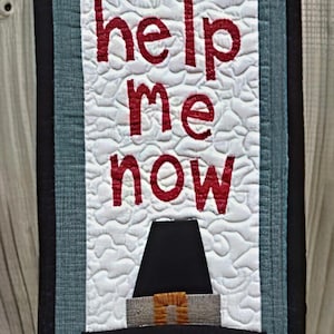Puede incluir: Colgante de pared acolchado con el texto "Oh Lord, help me now" en letras rojas. Un pavo con un sombrero de peregrino está en la parte inferior. El fondo es blanco con un patrón acolchado, enmarcado por tela azul y negra.