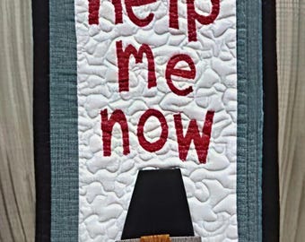 Puede incluir: Colgante de pared acolchado con el texto "Oh Lord, help me now" en letras rojas. Un pavo con un sombrero de peregrino está en la parte inferior. El fondo es blanco con un patrón acolchado, enmarcado por tela azul y negra.