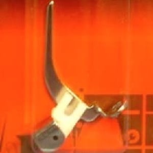 May include: A silver sewing machine foot with a curved needle and a white plastic piece.