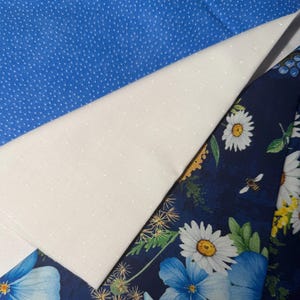 May include: An assortment of fabrics in shades of blue and white. One fabric is a solid blue with small white polka dots. Another is a white fabric with small white polka dots. The third fabric is a dark blue floral print with daisies and blue flowers.