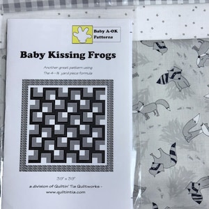 May include: A quilt pattern named "Baby Kissing Frogs" with a geometric design in black, white, and grey. The pattern is 99cm x 99cm and includes the text "Baby A-OK Patterns". The background fabric features a grey and white fox print.