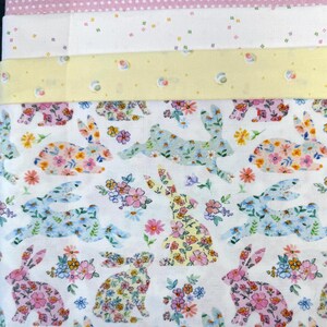 May include: A stack of colorful fabric pieces. The top fabric is pink with white polka dots. Below are fabrics with small floral and geometric patterns. The bottom fabric features bunny silhouettes filled with floral designs in pink, blue, and yellow.