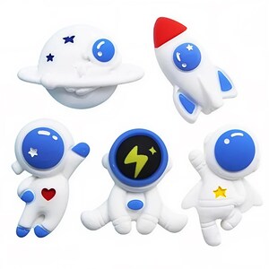 May include: A collection of white space-themed figurines, including a planet, rocket, and three astronauts. The planet has blue accents and stars. The rocket has a red tip. The astronauts have blue visors and various details like a heart and star.