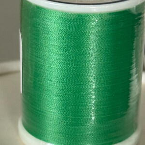 May include: A spool of bright green polyester thread, labeled with the number 645. The thread is tightly wound on a white plastic spool, with text indicating the thread is 60 wt. and 1,420 yards. The thread is for sewing and crafting.