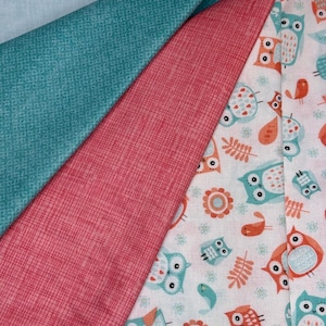 Peut inclure: Divers tissus aux motifs colorés. Un tissu turquoise clair avec un motif géométrique discret. Un autre est rouge corail avec un aspect texturé. Le troisième tissu présente des hiboux, des oiseaux et des éléments floraux sur fond blanc.