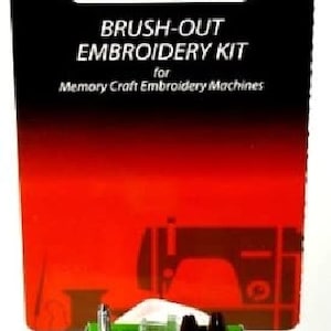 Könnte beinhalten: Eine grüne Box mit einem weißen Etikett, auf dem "Janome Brush-Out Embroidery Kit for Memory Craft Embroidery Machines" steht. Die Box enthält eine kleine Bürste, eine Nadel und einen Spulenwickler.