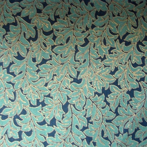 May include: Close-up of a fabric with a repeating leaf pattern. The leaves are teal with gold-colored outlines, set against a dark blue background. The design is detailed and creates a textured appearance.