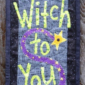 May include: A black and green quilted wall hanging with the text "That's Ms. Witch to You" in yellow and green lettering. A purple witch's hat with yellow stars is at the bottom of the hanging.