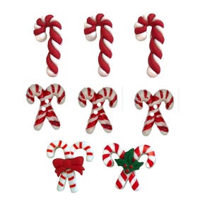 May include: A collection of Christmas-themed candy cane buttons in red and white. Some buttons are single candy canes, while others are crossed. One pair has a red bow, and another has green holly.