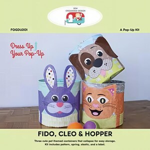 May include: Three pop-up containers with pet faces: a dog, a cat, and a bunny. The containers are cylindrical and decorated with colorful details. The text "Dress Up Your Pop-Up" and "FIDO, CLEO & HOPPER" are visible.
