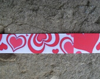 May include: White ribbon with a repeating pattern of red hearts. The hearts are in various sizes and shapes, some are outlined in white.