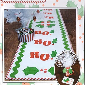 Könnte beinhalten: Weißer Weihnachtstischläufer mit rotem und grünem Stechpalmen-Design und den Worten "HO HO HO" in Rot. Der Läufer hat einen grünen, gewellten Rand und einen rot-weiß gestreiften Rand. Der Text "Ho Ho Holly Projects" steht oben.
