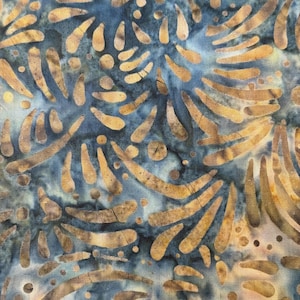 May include: Close-up of a fabric with a batik design. The fabric features a blue background with a pattern of tan, teardrop-shaped and curved elements. The design has a mottled appearance, with variations in color and texture.