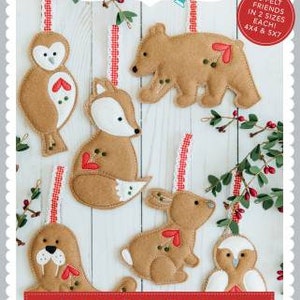 May include: Six felt animal ornaments with red hearts, including an owl, fox, bear, bunny, and two seals. The ornaments are on a white wood background with red and white ribbon. The text "HEART-FELT FRIENDS" is at the bottom of the image. The text "FORMATS: ART, DST, EXP, HUS, JEF, PES, VIP, VP3, XXX" is below the title.