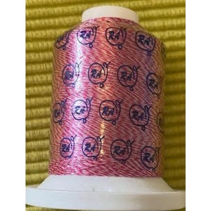 May include: A spool of pink and white thread with a metallic sheen. The spool is labeled with the text "RA" repeated many times.