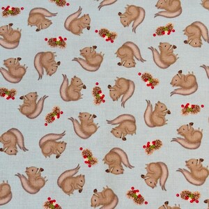 May include: A light blue fabric with a repeating pattern of brown squirrels holding nuts. The squirrels are surrounded by small red berries and brown pine cones.